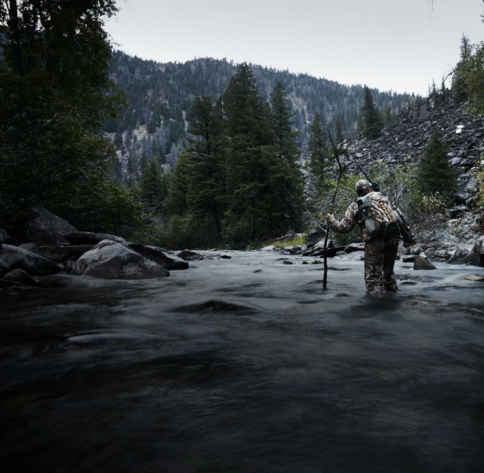 a man in hunting gear walking in a creek.