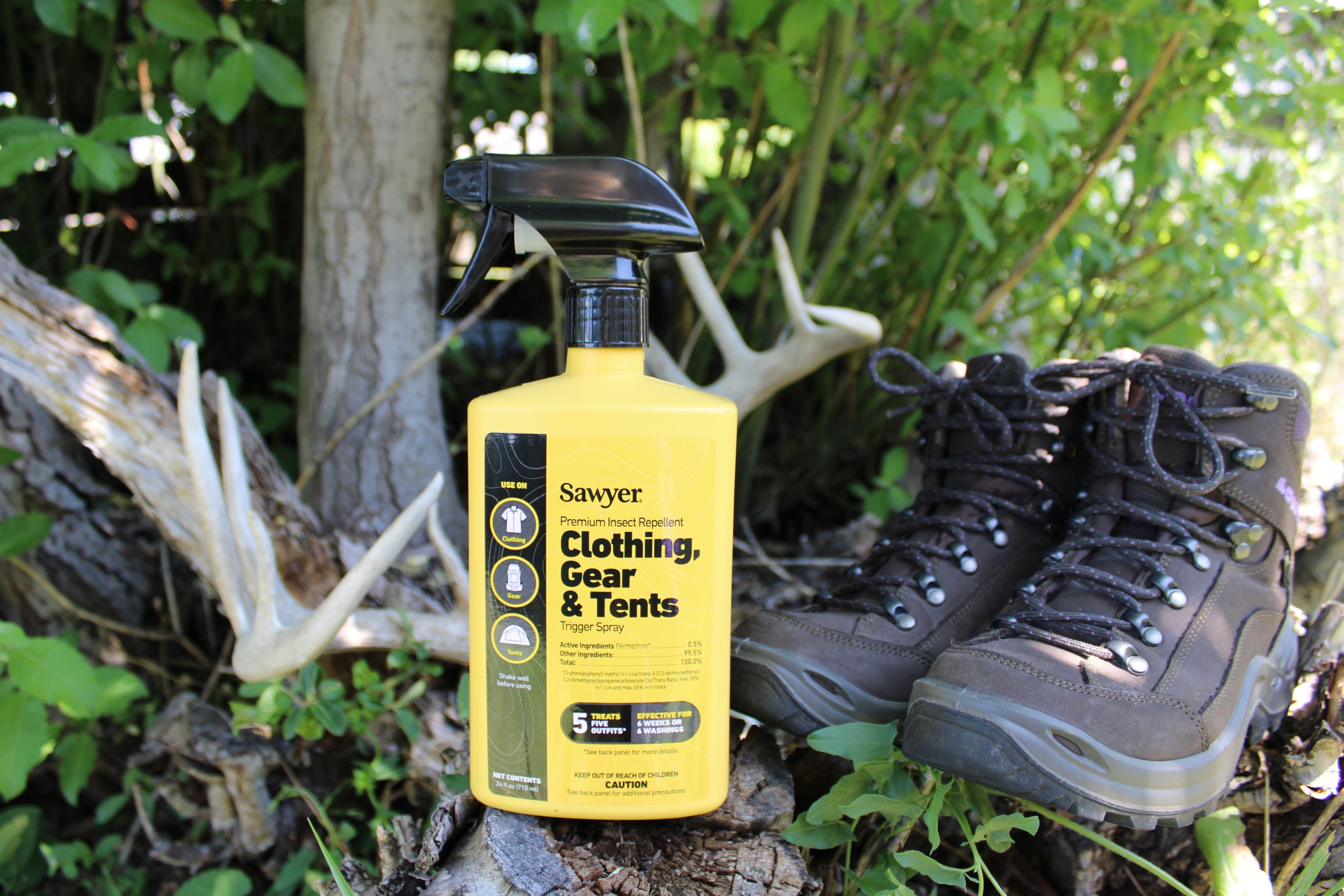Sawyer permethrin spray bottle sits beside hiking boots treated with the spray