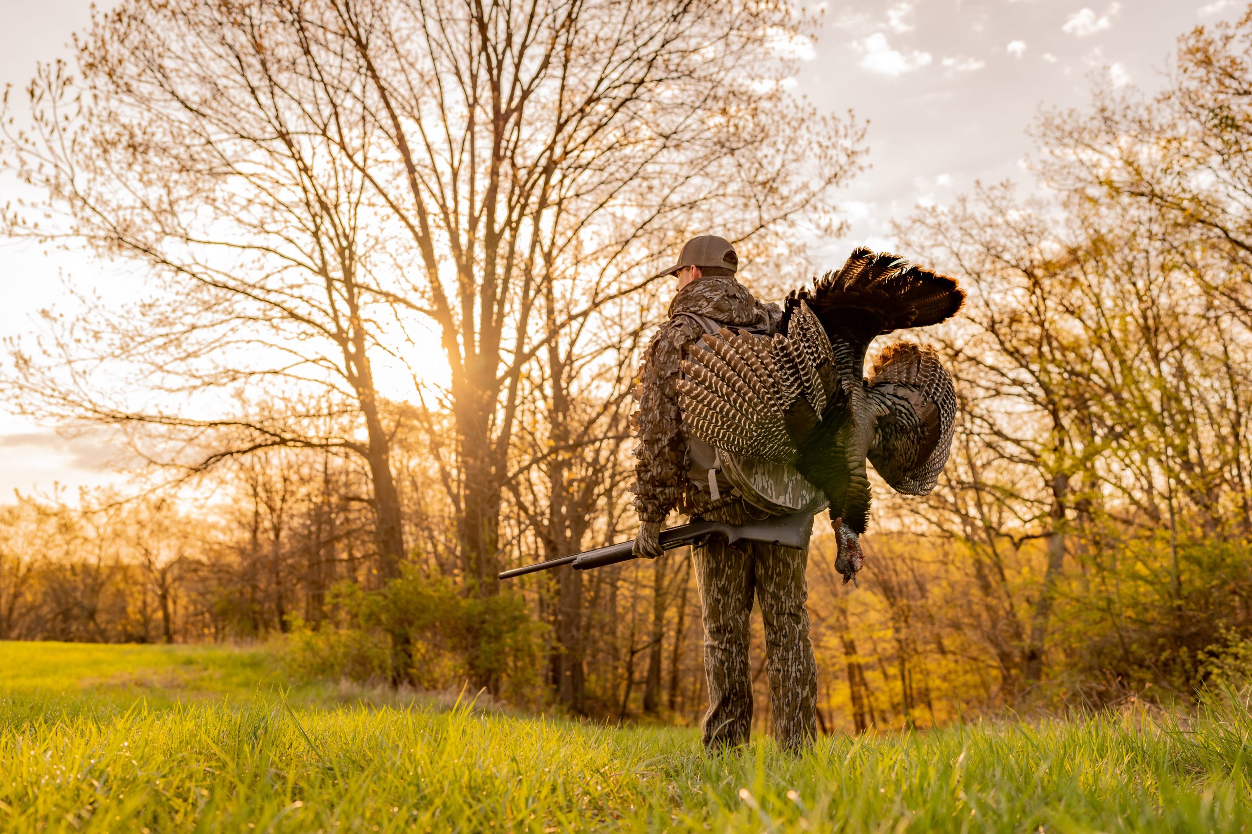 Hunter stands with his harvested turkey looking at the sunset