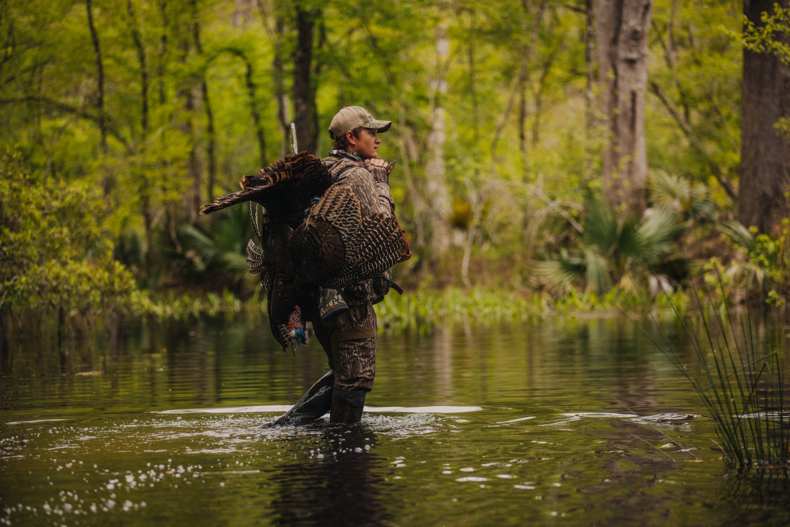 A hunter crosses a stream with a harvested gobbler.