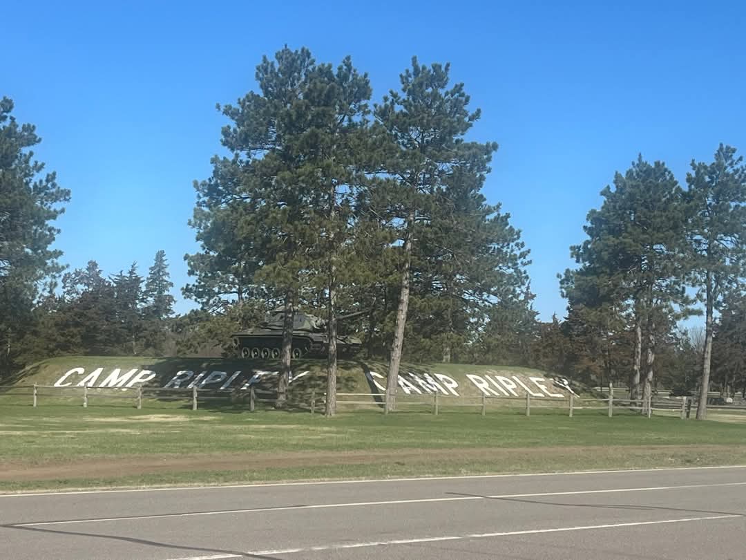 A roadside view of the entrance to Camp Ripley, featuring large white letters spelling “CAMP RIPLEY” on a grassy embankment.